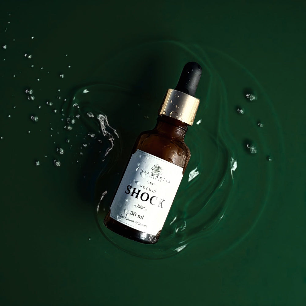 Anja Marija SHOCK serum – 30 ml brown glass dropper bottle with a gold cap, floating on a dark green water surface with ripples and droplets, natural skincare aesthetic.